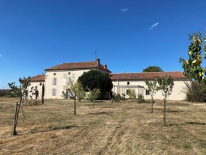 A large, single-story building with a red-tiled roof and a beige facade, surrounded by dry grass and sparse trees. - Le Gîte de Font Valet (Millac)