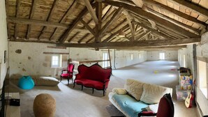 An open-plan room with a high wooden ceiling, a red armchair, a blue bean bag, and a sofa with pillows. - Le Gîte de Font Valet (Millac)