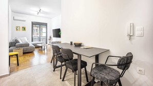 A modern living room with a grey sofa, a small round table, and a dining table with four chairs. - Modern 2BR in Exarchia | Ensuite Baths & Workspace (Athina)