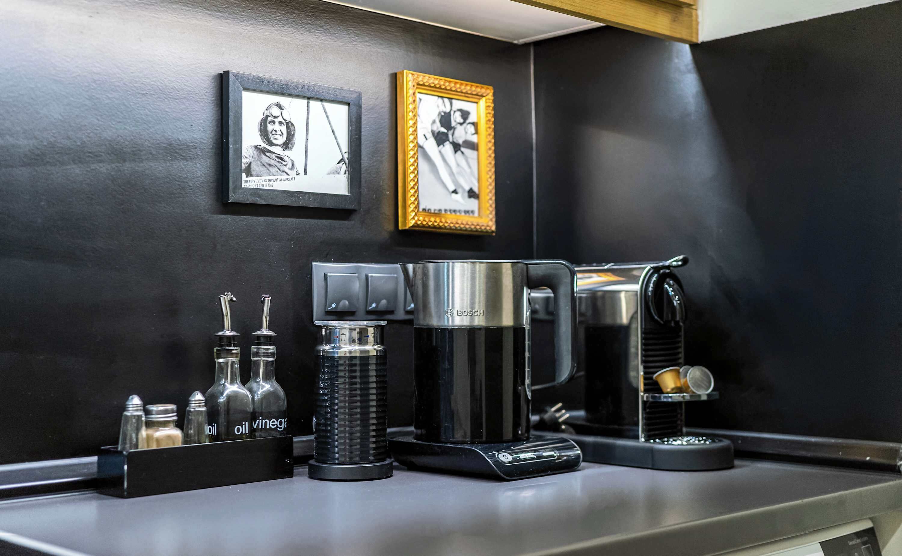 Eine Kaffeestation mit einer Bosch-Kaffeemaschine, Salz- und Pfefferstreuern sowie Öl- und Essigflaschen. Darüber hängen zwei gerahmte Bilder an der Wand.
