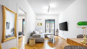 A modern living room with a sofa, coffee table, and a TV. - Modern 2BR in Exarchia | Ensuite Baths & Workspace (Athina)