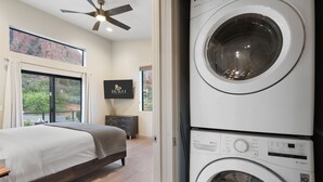 A bedroom with a bed, a ceiling fan, a large window with curtains, and a washing machine. - Moondance @ Oak Creek | Townhouse w/Views| FirePit (Sedona)