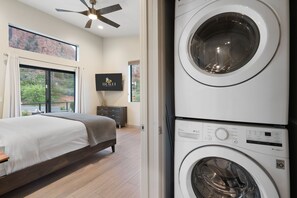 A bedroom with a bed, a ceiling fan, a large window with curtains, and a washing machine.