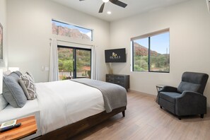 Ein Schlafzimmer mit Bett, Fernseher, Sessel und großen Fenstern mit Blick auf rote Felsformationen.