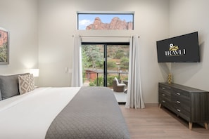 Un dormitorio con una cama grande, un televisor montado en la pared, un ventanal corredero que da a un espacio exterior y un aparador de madera oscura.