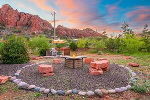 A fire pit surrounded by rocks and greenery, with a view of red rock formations in the background. - Cimaron Butte Studio | Kitchenette & Laundry (Sedona)