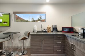 A modern kitchen with a built-in microwave, coffee maker, and a window with a scenic view. - Cimaron Butte Studio | Kitchenette & Laundry (Sedona)