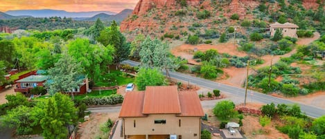 Una casa con techo rojo, rodeada de vegetación y una carretera, con montañas al fondo.