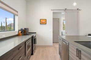 A modern kitchen with a large window, a dishwasher, and a sliding door leading to another room.