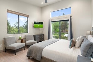 Un dormitorio con una cama grande, dos sillones, un televisor y vistas a árboles y un campo de golf.