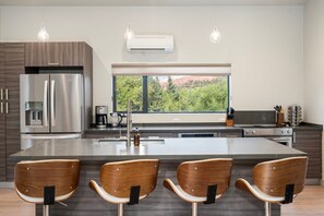 A modern kitchen with a central island, stainless steel appliances, and a large window overlooking greenery. - Cimaron Butte View Terrace | 2 Kings | FirePit (Sedona)