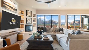 A modern living room with a flat-screen TV, a ceiling fan, and a large window offering a mountain view. - Sycamore Canyon Luxe Retreat | 180° Views + Hottub (Sedona)