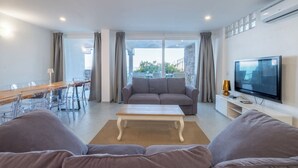 A modern living room with a sofa, coffee table, TV, and dining area with chairs and a table. - HT RTA Sole Dell'Argentario (Porto Santo Stefano)
