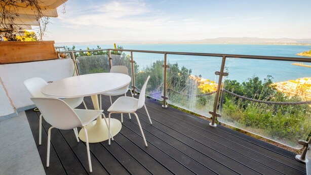 A balcony with a round table and four chairs, overlooking a body of water and distant land. - HT RTA Sole Dell'Argentario (Porto Santo Stefano)