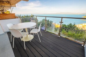 Un balcone con un tavolo rotondo e quattro sedie, affacciato su uno specchio d'acqua e la terraferma in lontananza.