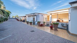 A hotel corridor with a brick pathway, potted plants, and a motorbike parked by the entrance. - HT RTA Sole Dell'Argentario (Porto Santo Stefano)