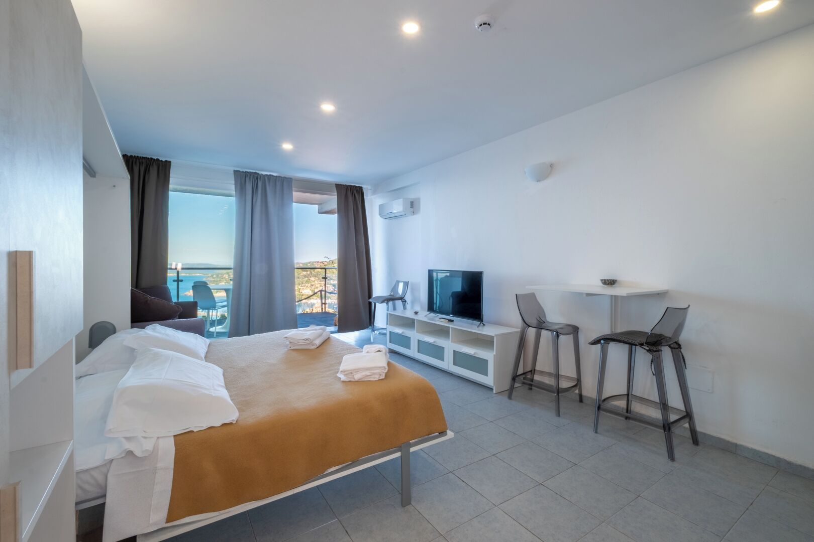 Una habitación de hotel moderna con cama, televisor, escritorio y balcón con vistas.