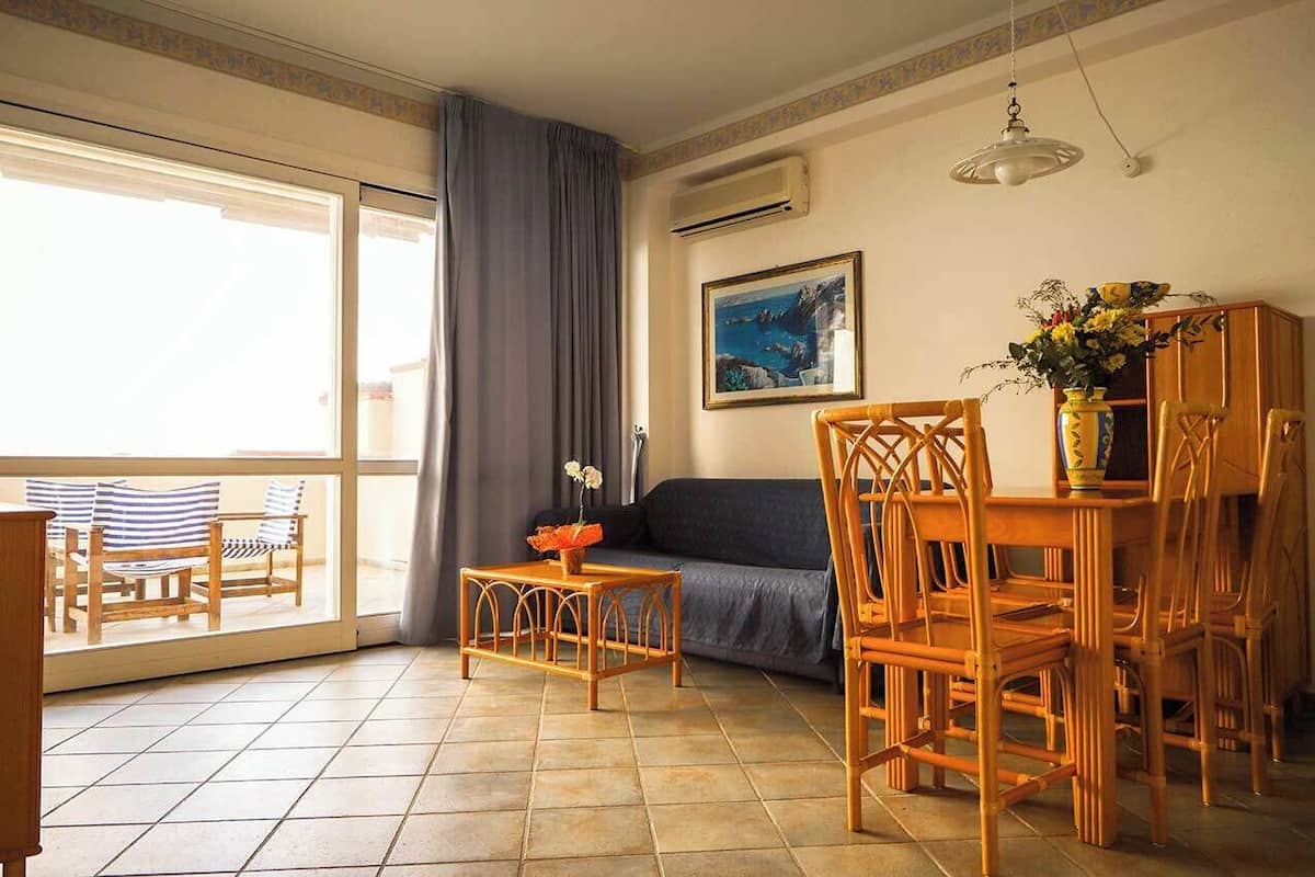 Un soggiorno con divano, poltrone, un tavolo e un balcone con sedie.