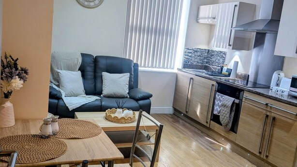 Ein modernes Wohnzimmer mit einem schwarzen Ledersofa, einem Holzesstisch mit Stühlen und einer Küchenzeile mit Schränken und einem Herd.
