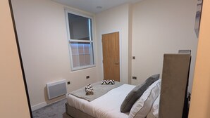 Ein Schlafzimmer mit Bett, Fenster, Heizkörper, Tür und Nachttisch mit Lampe.