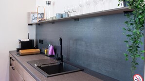 A modern kitchen with a built-in sink, a wooden countertop, and a shelf above holding wine glasses and a framed picture. - Apartment in Koblenz near Deutsches Eck (Koblenz)