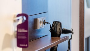 A hairdryer plugged into a wall socket on a wooden shelf. - Premier Inn Hamburg City Zentrum (Hamburg)