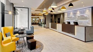 A hotel lobby with a reception desk, seating area with chairs, and pendant lighting.