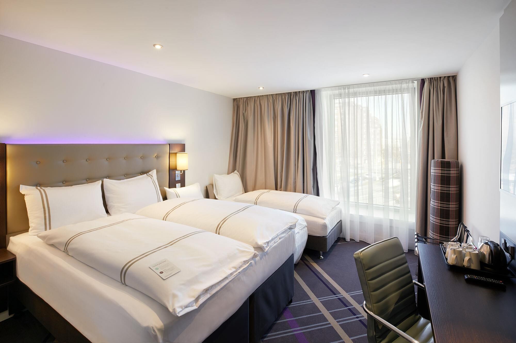Ein Hotelzimmer mit zwei Betten, einem Schreibtisch mit Stuhl, einer Lampe und einem Fenster mit Vorhängen.