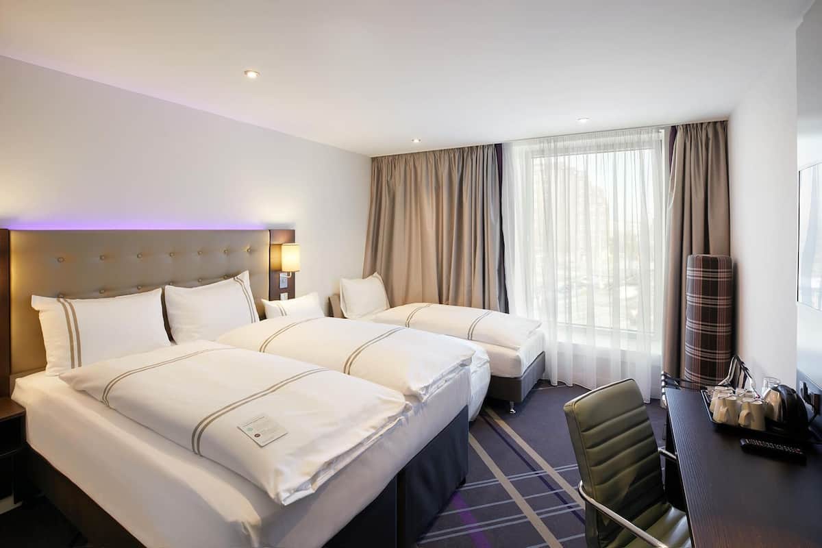 A hotel room with two beds, a desk with a chair, a lamp, and a window with curtains.