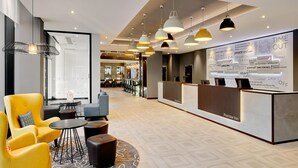 A hotel lobby with a reception desk, seating area with chairs, and pendant lighting. - Premier Inn Hamburg City Zentrum (Hamburg)