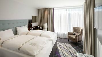 Habitación de hotel con dos camas, una silla, un televisor y un ventanal grande con cortinas.