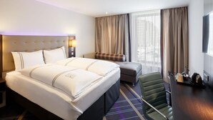 A hotel room with a large bed, a desk with a chair, a TV, and a window with curtains.
