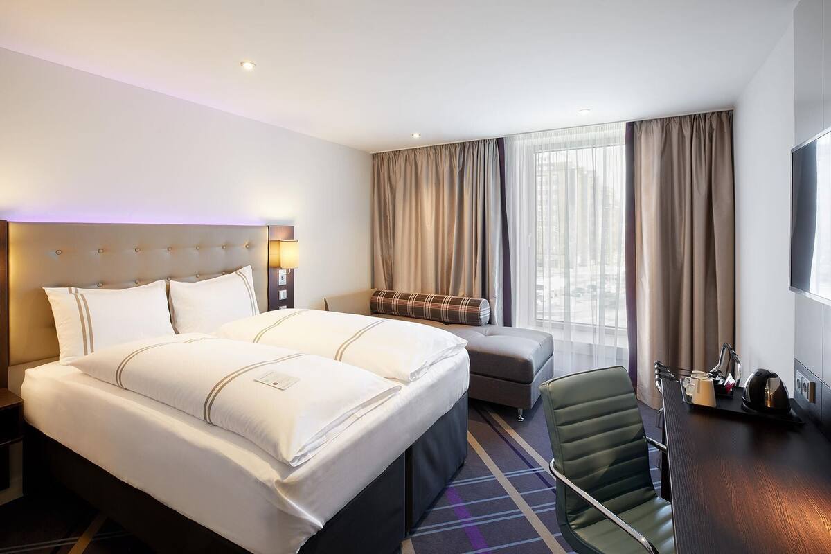 A hotel room with a large bed, a desk with a chair, a TV, and a window with curtains.