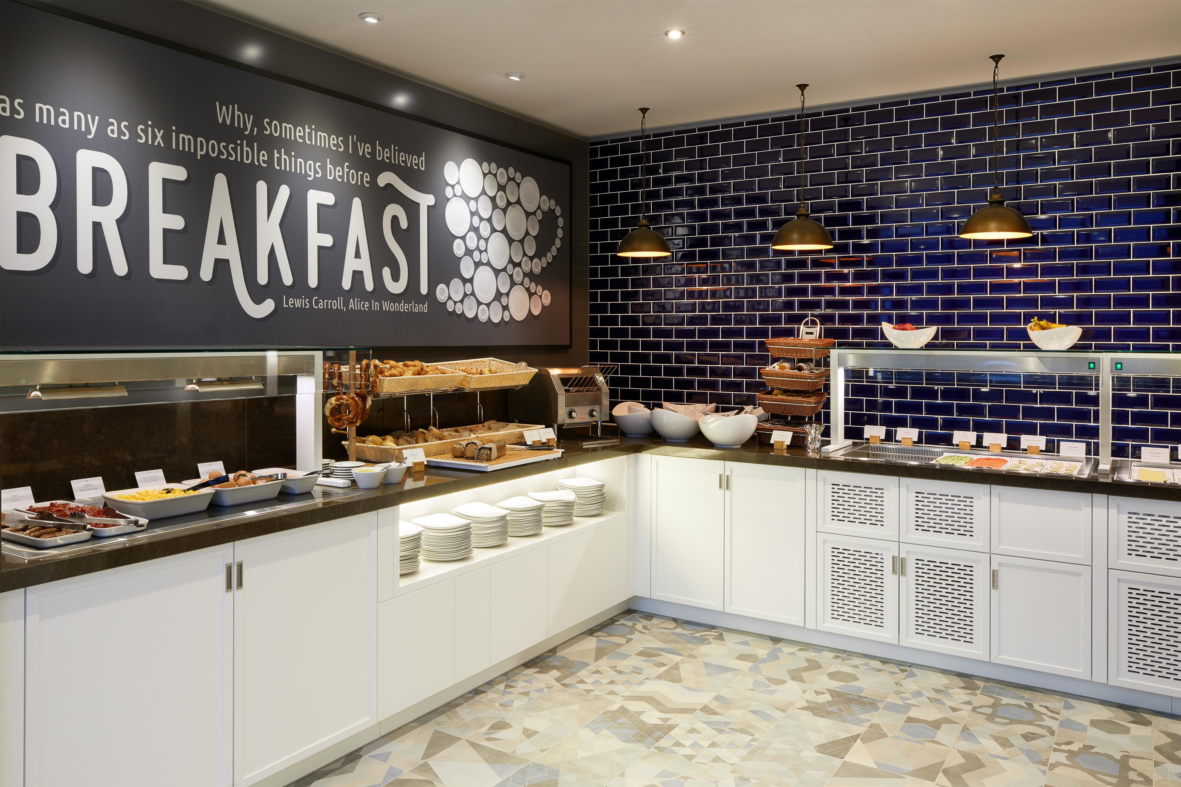 A breakfast buffet with various food items, a wall with a quote, and a blue-tiled backsplash.