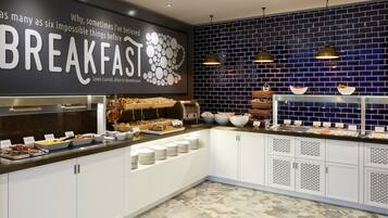 A breakfast buffet with various food items, a wall with a quote, and a blue-tiled backsplash.