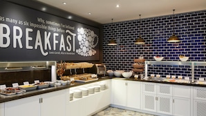 A breakfast buffet with various food items, a wall with a quote, and a blue-tiled backsplash.