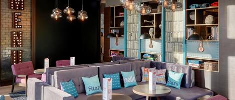 A modern lounge area with sofas, tables, and a bookshelf with various items.