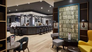 A modern bar area with a counter, bar stools, and a bookshelf with books. - Premier Inn Hamburg City Zentrum (Hamburg)