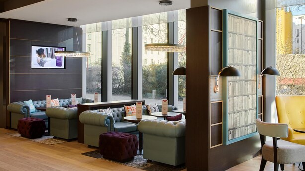 A modern lounge area with sofas, ottomans, a bookshelf, and a television.