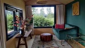 Ein gemütliches Wohnzimmer mit großem Fenster, einem grünen Sofa, einer hölzernen Bank und einer dekorativen Vase mit Blumen.