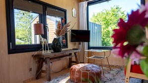 Ein gemütliches Zimmer mit einem Holztisch, einem Fernseher, einem Fenster mit Blick auf Grünflächen und einem farbenfrohen Teppich.