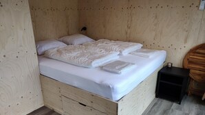 A wooden bed with two pillows and a blanket, a small bedside table, and a wooden dresser. - Cabin in Nature near Scenic Trails (Scherpenzeel (FR))