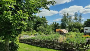 A garden with a wooden fence, a white trailer, and various plants. - Cabin in Nature near Scenic Trails (Scherpenzeel (FR))