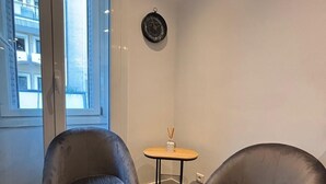 Une pièce d’angle avec deux fauteuils en cuir foncé, une petite table en bois sur laquelle est posée une bougie, et une horloge murale.