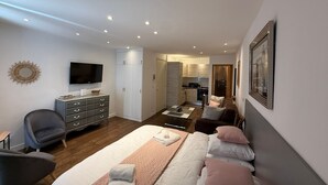 Une chambre à coucher moderne avec un lit, une télévision, une commode et, au fond, un coin cuisine.