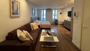 Une chambre d’hôtel moderne avec un canapé marron, un lit près d’une grande fenêtre, un bureau avec une chaise et un téléviseur à écran plat.