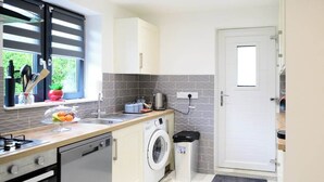A compact kitchen with a washing machine, a sink, and a window with blinds.