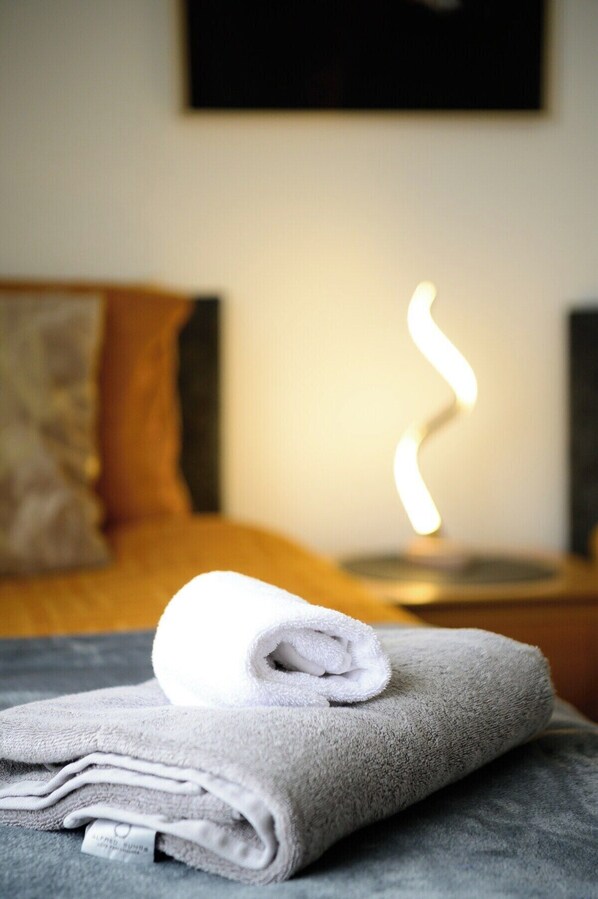 Une serviette soigneusement pliée sur un lit, avec une source de lumière chaude en arrière-plan.