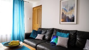 A living room with a black leather sofa, a wooden door, and a framed abstract painting on the wall.