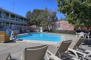 Una piscina con sillones de descanso, un edificio con balcones y un muro de ladrillo.